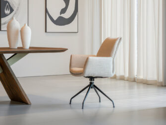 Comfortabele eetkamerstoel met elegante draaipoot in zwart metaal en afgeronde armleuningen in warme zandkleurige bekleding